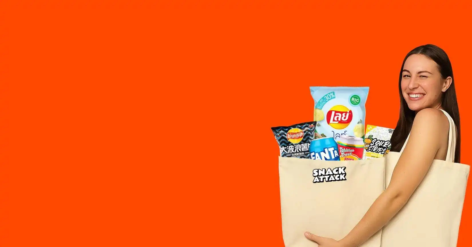 A smiling woman holding a reusable shopping bag filled with snacks and drinks.